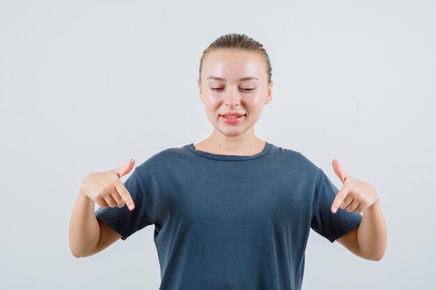 Jeune femme pointant vers le bas et souriant en t-shirt gris