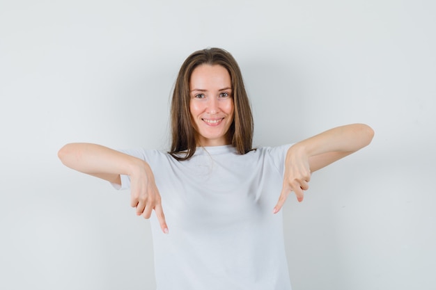 Jeune femme pointant vers le bas en t-shirt blanc et à la confiance
