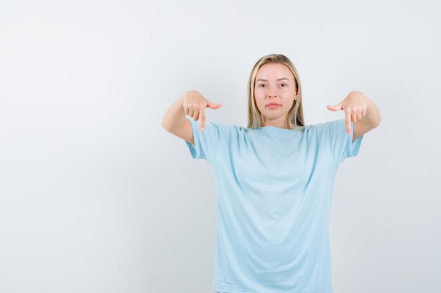 Jeune femme pointant vers le bas en t-shirt et à la confiance isolée