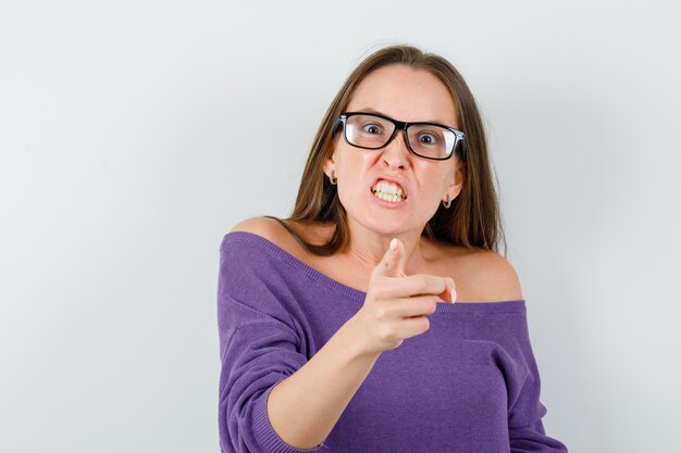 Jeune femme pointant vers la caméra en chemise de laine et à la nervosité. vue de face.