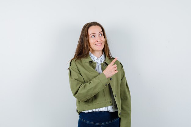 Jeune femme pointant vers le coin supérieur droit en chemise, veste et à la recherche de rêve. vue de face.