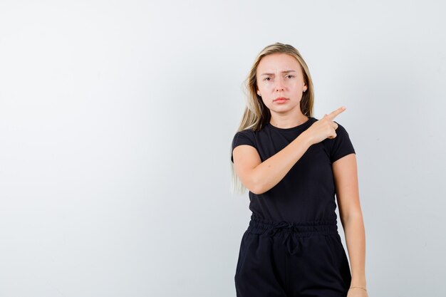 Jeune femme pointant vers le coin supérieur droit en t-shirt, pantalon et regardant malade. vue de face.