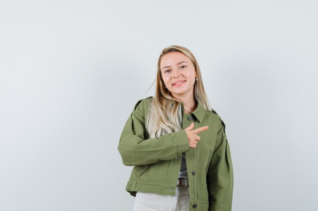 Jeune femme pointant vers le coin supérieur droit en veste, pantalon et à la joyeuse. vue de face.