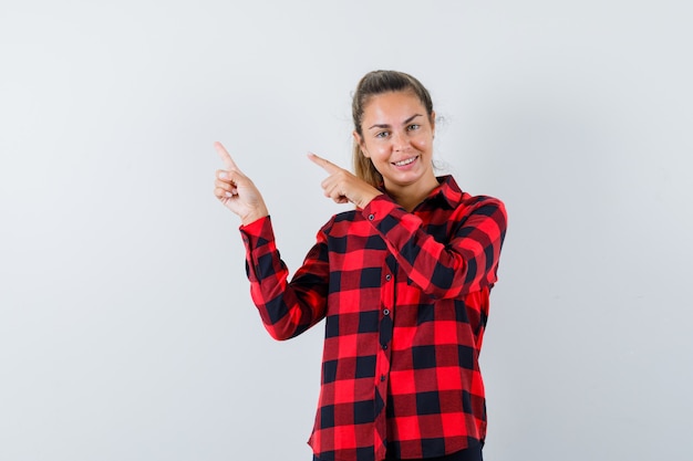 Jeune femme pointant vers le coin supérieur gauche en chemise à carreaux et à la bonne humeur