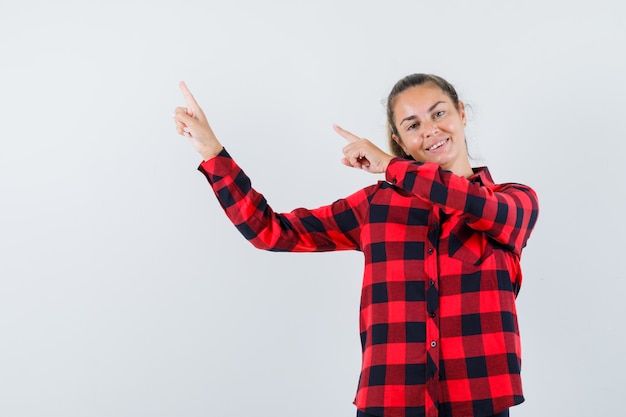 Jeune Femme Pointant Vers Le Coin Supérieur Gauche En Chemise à Carreaux Et à La Bonne Humeur