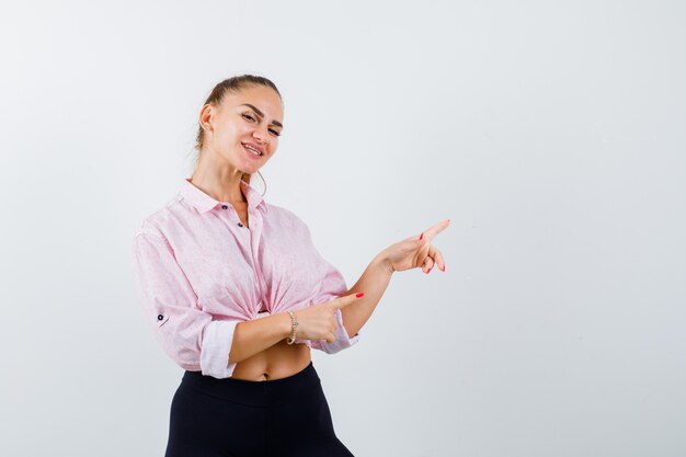 Jeune femme pointant vers le côté droit en chemise décontractée et à la joyeuse vue de face.