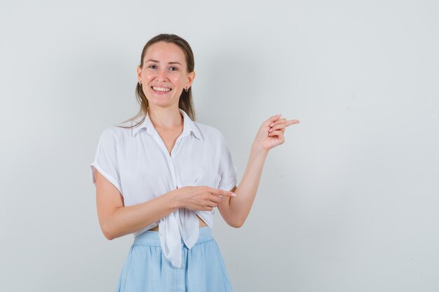 Jeune femme pointant vers le côté droit en chemisier, jupe et à la joyeuse