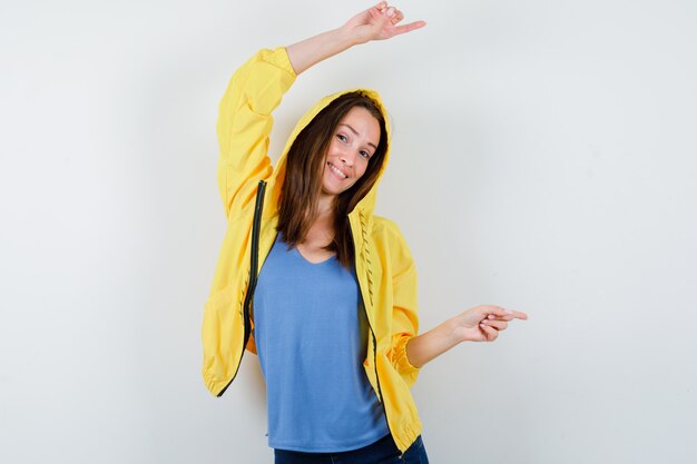 Jeune femme pointant vers le côté droit en t-shirt, veste et l'air confiant, vue de face.