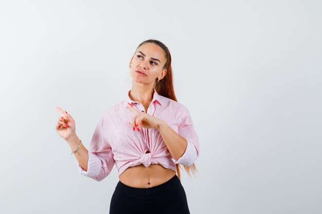 Jeune femme pointant vers le côté gauche en chemise décontractée et à la recherche attentionnée. vue de face.