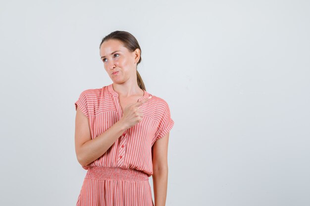 Jeune femme pointant vers le côté et regardant ailleurs en vue de face de robe rayée.