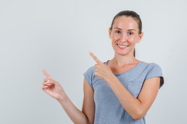 Jeune femme pointant vers le côté en t-shirt gris et à la joyeuse vue de face.