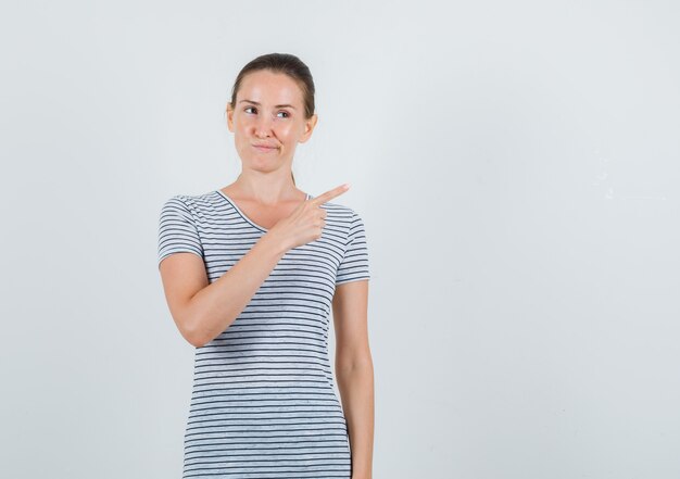 Jeune femme pointant vers le côté en t-shirt et regardant curieux, vue de face.