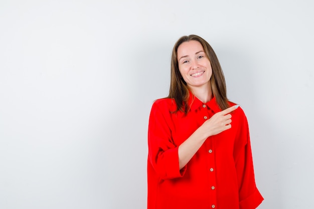 Jeune femme pointant vers la droite en blouse rouge et à la gaieté, vue de face.