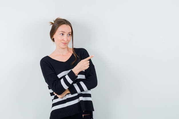 Jeune femme pointant vers la droite avec l'index en chemisier noir et pantalon noir et à heureux