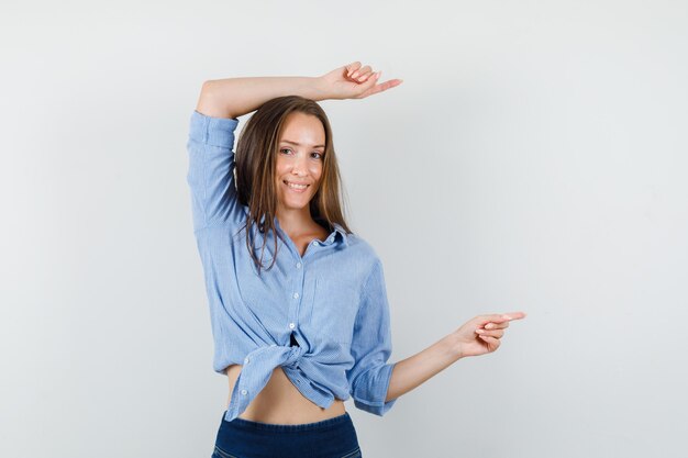 Jeune femme pointant vers l'extérieur en chemise bleue, pantalon et à la joyeuse