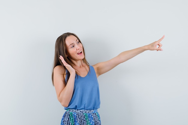 Jeune femme pointant vers l'extérieur en maillot, jupe et à la joyeuse, vue de face.