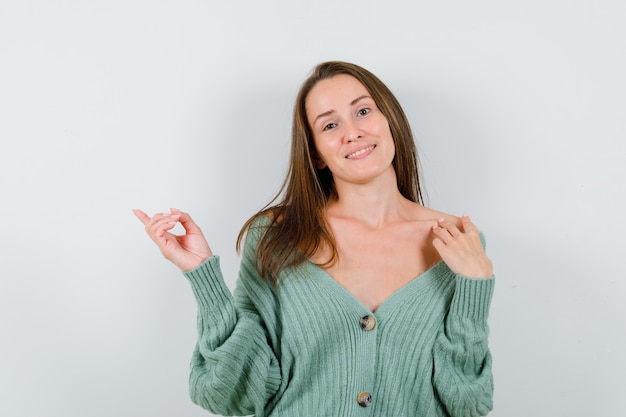 Jeune femme pointant vers la gauche en cardigan en laine et à la gaieté. vue de face.