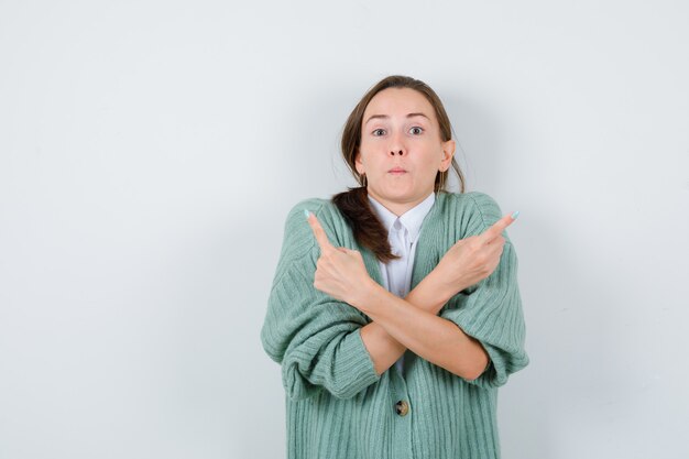 Jeune femme pointant vers la gauche et la droite en blouse, cardigan et à la perplexité , vue de face.