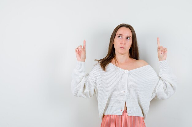 Jeune femme pointant vers le haut en cardigan et jupe à la recherche d'isolement pensive