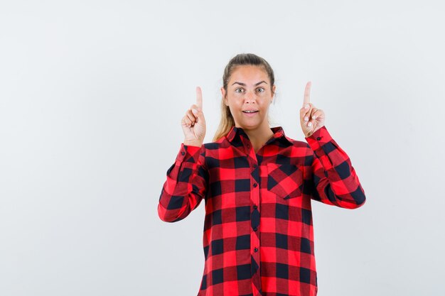 Jeune femme pointant vers le haut en chemise décontractée et à la recherche de bonheur. vue de face.