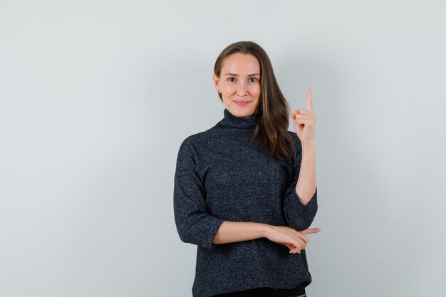 Jeune femme pointant vers le haut en chemise et à l'optimiste