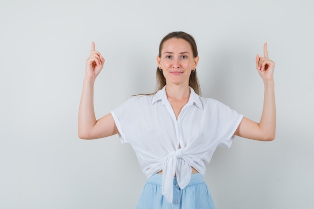 Jeune femme pointant vers le haut en chemisier et jupe et à la confiance