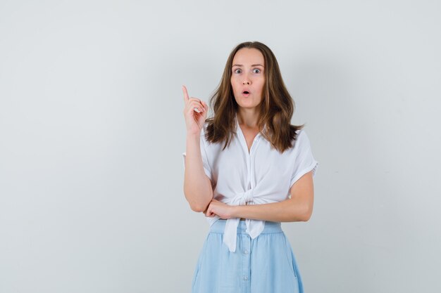 Jeune femme pointant vers le haut en chemisier et jupe et regardant anxieux