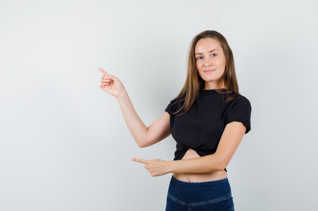 Jeune femme pointant vers le haut en chemisier noir, pantalon et à la confiance