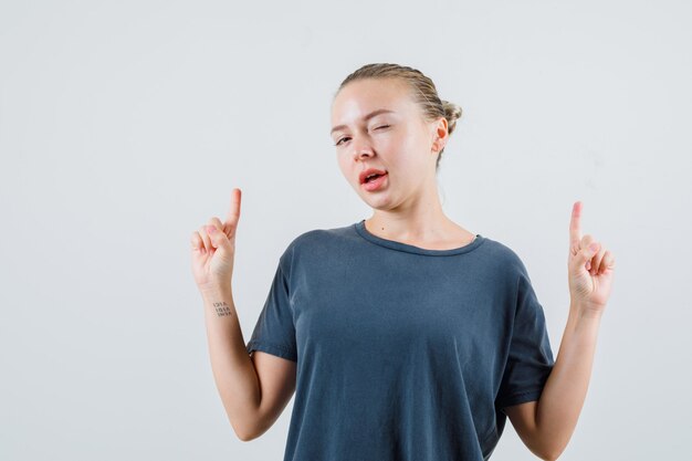 Jeune femme pointant vers le haut et clignant des yeux en t-shirt gris