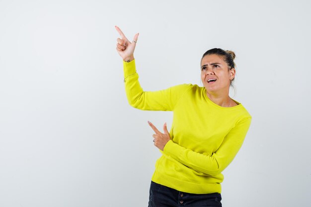 Jeune femme pointant vers le haut en pull jaune et pantalon noir et à l'accent