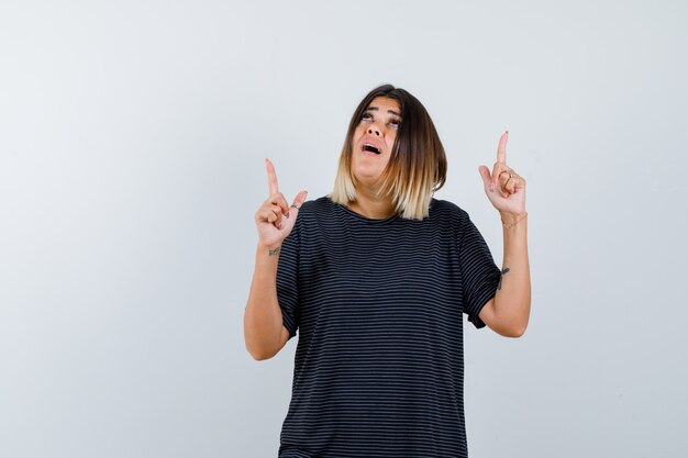 Jeune femme pointant vers le haut en robe de polo et à la perplexité. vue de face.