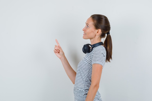 Jeune femme pointant vers le haut et souriant en t-shirt, casque.