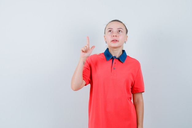 Jeune femme pointant vers le haut en t-shirt et à la recherche concentrée