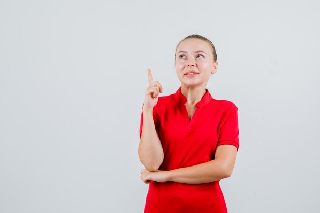 Jeune femme pointant vers le haut en t-shirt rouge et à la recherche d'espoir