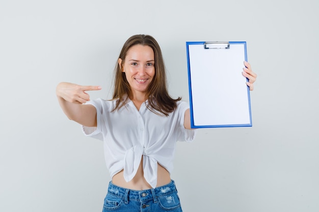 Jeune femme pointant vers le presse-papiers vierge en vue de face de chemisier blanc.