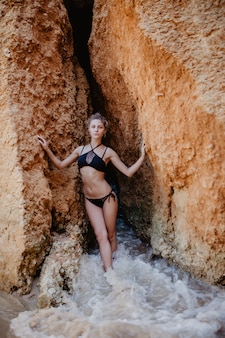 Jeune femme portant un bikini posant à l'heure d'été près des rochers