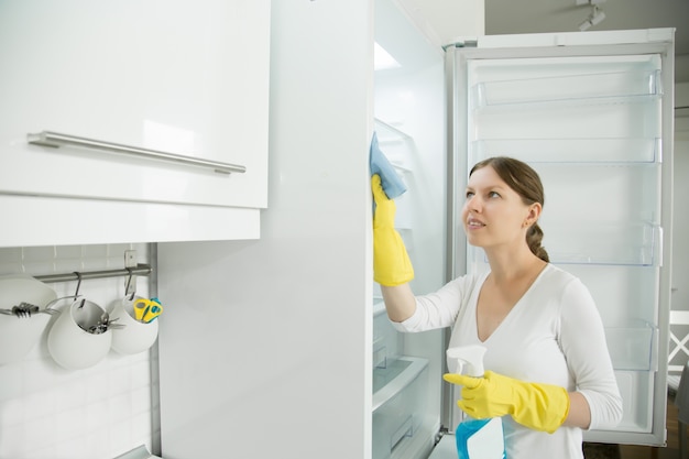 Jeune femme portant des gants en caoutchouc nettoyant le réfrigérateur