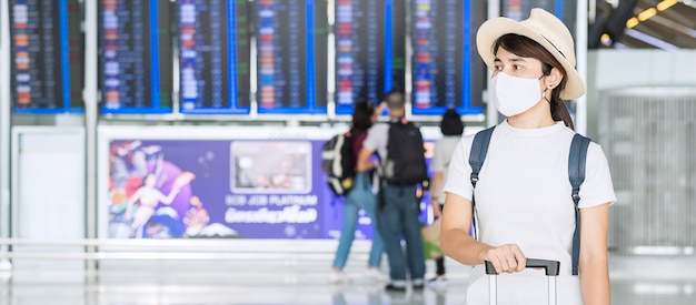 Jeune femme portant un masque facial avec bagages vérifier le temps de vol à l'aéroport