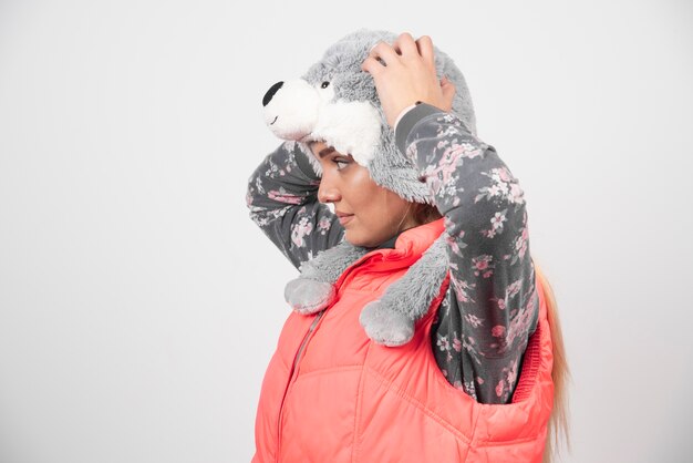 Jeune femme posant avec un chapeau drôle sur un mur blanc.