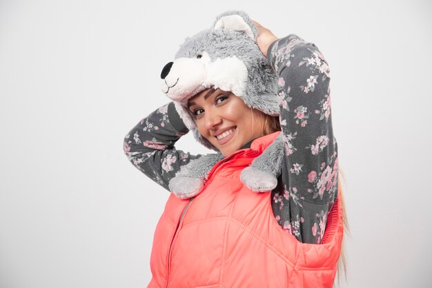 Jeune femme posant avec un chapeau drôle sur un mur blanc