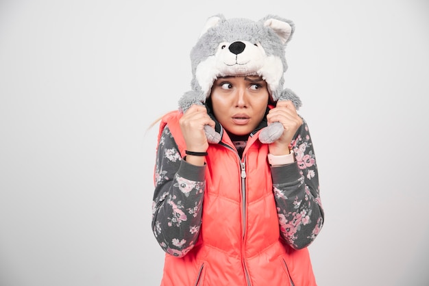 Jeune femme posant avec un chapeau drôle sur un mur blanc