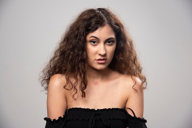 Jeune femme posant en chemisier noir aux cheveux bouclés. Photo de haute qualité