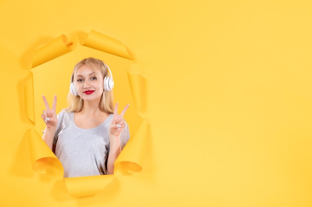 Jeune femme posant dans des écouteurs sur papier jaune déchiré fond audio ultrasons musique sonore