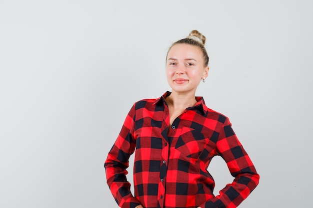 Jeune femme posant debout en chemise à carreaux et à la vue de face, confiant.