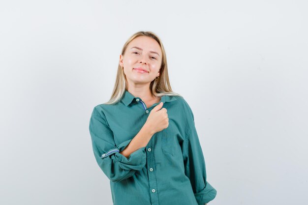 Jeune femme posant debout en chemise verte et semblant joyeuse.