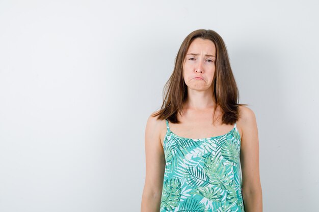 Jeune femme posant debout en chemisier et l'air offensé. vue de face.