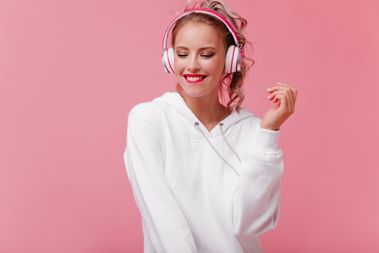Photo gratuit jeune femme posant et écoutant de la musique grâce à ses écouteurs roses