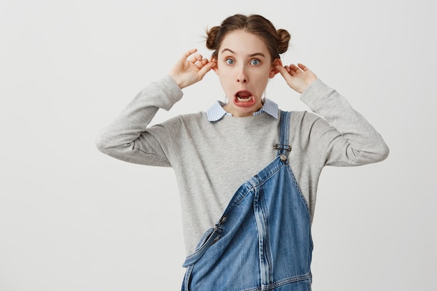 Jeune femme posant de façon ludique avec la bouche ouverte grimaçant s'amuser. Écolière dans des vêtements décontractés s'amusant à faire des oreilles saillantes au lieu d'étudier. Attitude, concept de position