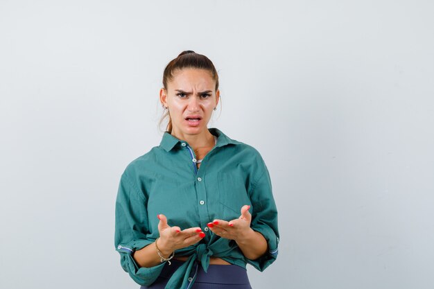 Jeune femme posant un geste de question en chemise verte et ayant l'air confus, vue de face.