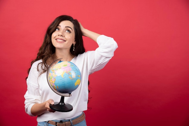 Jeune femme posant avec globe sur fond rouge. photo de haute qualité